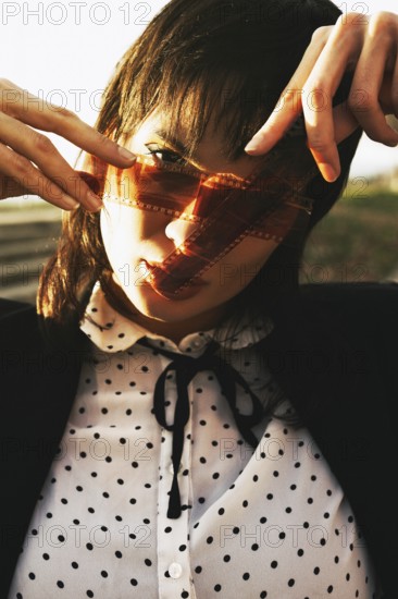 Woman in polka dot blouse, holding film strip against sunlight, creating an artistic shadow over