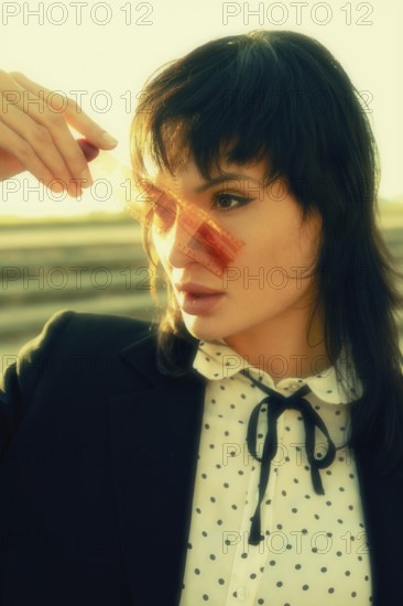 Woman holding a film strip against a sunlit background. She wears a polka dot blouse and black
