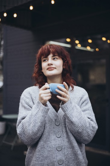 A young woman enjoys a coffee in a cafe terrace, wearing a cozy sweater, surrounded by string