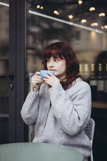 A young woman in a cozy sweater enjoys her coffee on a cafe terrace. The ambiance is warm, with a