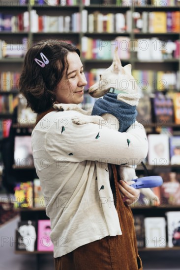 A young woman holds her dog lovingly in a warm bookstore, surrounded by colorful books. The cozy