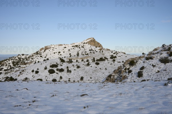 A serene winter scene at Montcabrer in Spain, showcasing its snow-capped peak under a clear blue