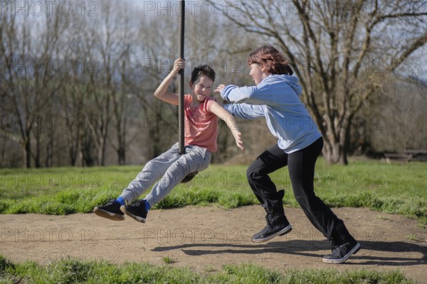Two friends enjoy a sunny day by playing on a zip line in a park. Laughter and joy fill the air as