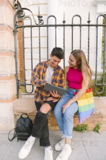 A happy lesbian couple sits outdoors looking at a digital tablet, symbolizing love, equality, and