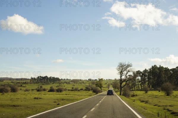 A car travels along a quiet country road under a clear blue sky on a peaceful autumn morning The