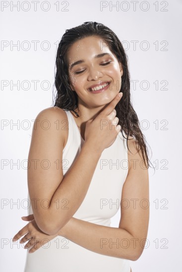 Studio portrait of a joyful female model with wet hair and skin, her eyes gently closed, wearing a
