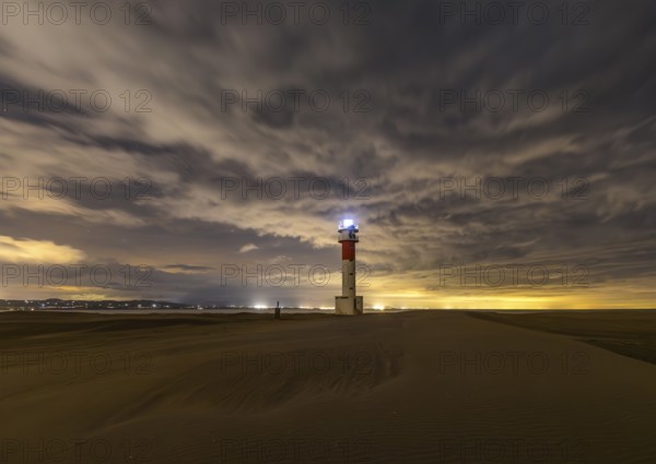 Fangar Lighthouse in Tarragona, Spain stands alone on sandy dunes under a dramatic sky The