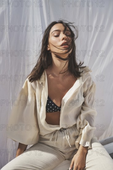 A woman enjoys the summer sun, dressed in a stylish cream blouse and polka dot bikini top The