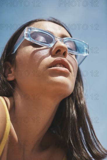 A fashionable woman sporting trendy, clear blue sunglasses basks under the vibrant summer sky Her