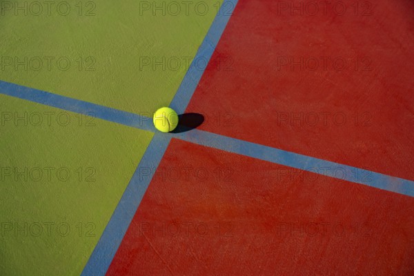 Close-up view of a yellow tennis ball at the intersection of colorful court lines, showcasing the