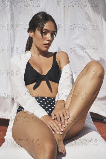 A woman enjoys the summer sunshine on a rooftop, wearing a black and polka-dot swimsuit The scene