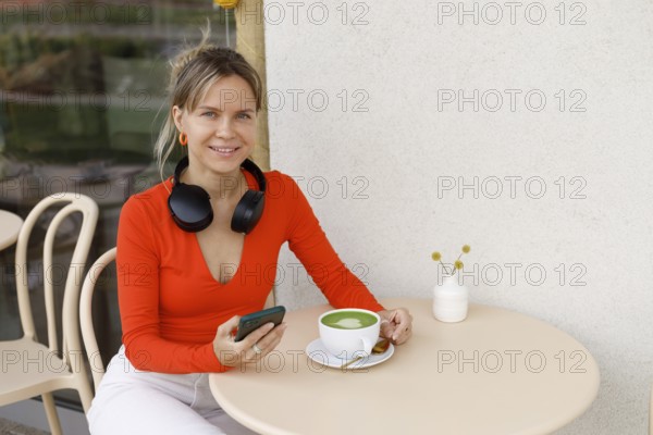 Smiling woman in a bright orange top sits at a Warsaw cafe table She wears headphones around her