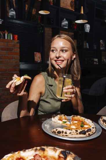 A cheerful person enjoys a slice of Margherita pizza paired with a glass of refreshing citrus