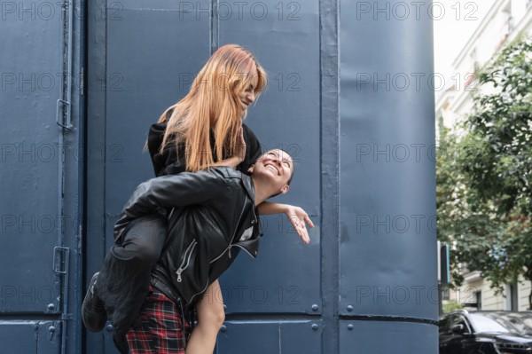 A joyful lesbian couple shares a playful piggyback ride in an urban setting, laughing and enjoying