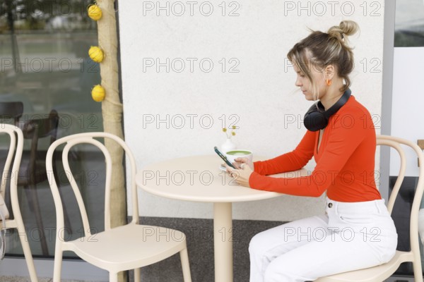 A woman in a vibrant orange top sits at an outdoor cafe in Warsaw, using her smartphone with