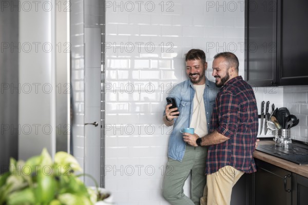 A happy gay couple stands in a bright kitchen, sharing a joyful moment while looking at a
