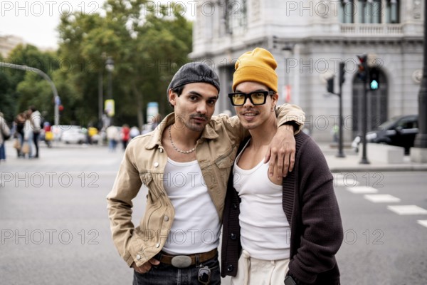A Colombian gay couple stands joyfully in an urban setting. They wear casual outfits, expressing a
