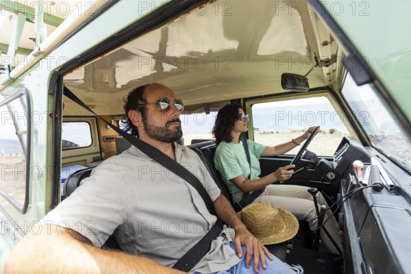 A blind man relaxes in a motorhome while a woman drives. The scenic coastal setting enhances the
