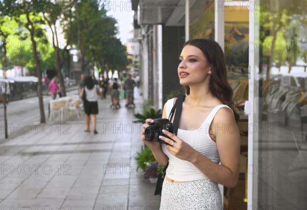 A young woman stands on a bustling city street, holding a camera Surrounded by passersby, she