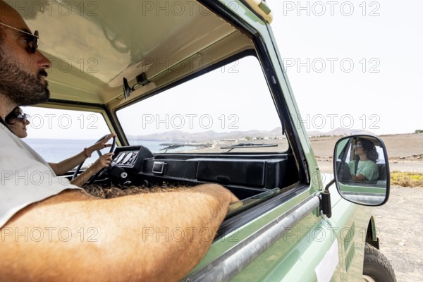 A blind man and a woman drive a motorhome along a coastal road with scenic mountains in the