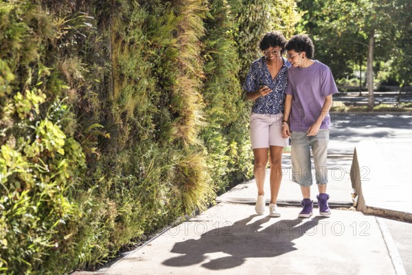 A loving multiethnic LGBTQ+ couple smiles as they enjoy a sunny day, walking side by side along a