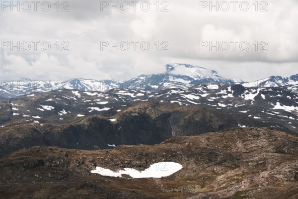 A stunning view of Norway's rugged mountains, dotted with patches of snow The dramatic clouds and