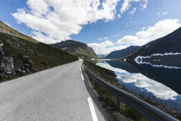A stunning road in Norway stretches into the distance, flanked by majestic mountains and a