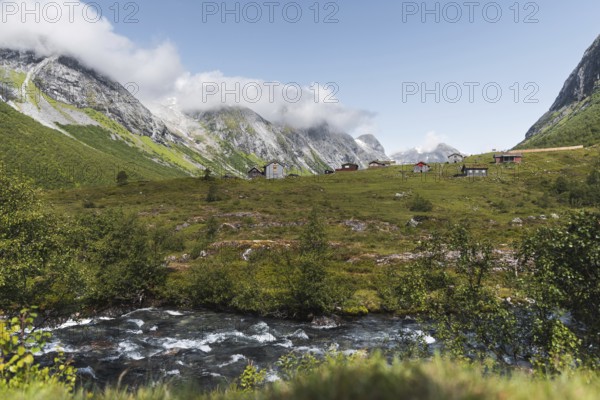 A serene mountain village nestled in a lush green valley in Norway, surrounded by towering peaks