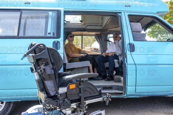 Two men sitting inside a blue van that's adapted for wheelchair access, with the wheelchair