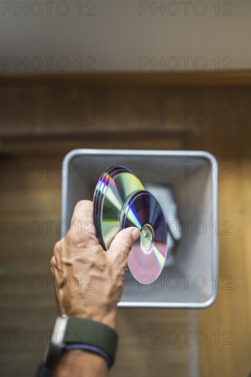 A person hand dropping assorted DVDs into a trash bin. The image highlights the decline of physical