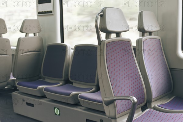 A row of empty train seats with purple upholstery and patterned design by a window. The setting