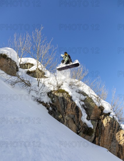 A daring snowboarder leaps off a snowy cliff, showcasing thrilling winter sports skills against a