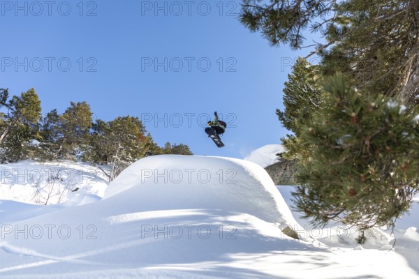 A snowboarder soars through the clear blue sky, performing an aerial trick above a snowy mountain