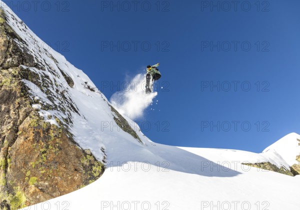 A snowboarder performs an impressive jump off a snow covered mountain, leaving a trail of snow