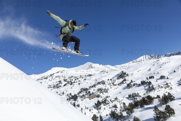 Snowboarder performs a jump on snowy mountain slope, surrounded by a breathtaking winter landscape.