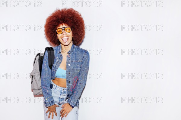 Joyful African descent woman with voluminous afro hair, sticking out her tongue, wearing