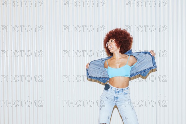 A joyful African descent woman with voluminous afro hair wearing light blue denim jeans, a crop