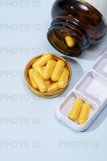Top view of a dark amber bottle spilling yellow capsules into a gold lid, alongside a white pill