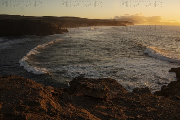 Dramatic view of powerful waves hitting rugged rocks with a sunset backdrop at La Pared,