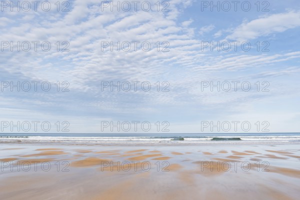 A tranquil beach scene featuring an expansive view of gentle waves under a sky filled with soft
