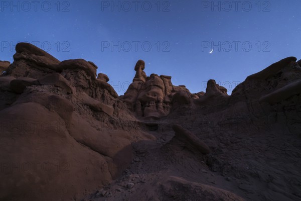 A serene night view of sandstone formations under a starry sky with a crescent moon in Goblin