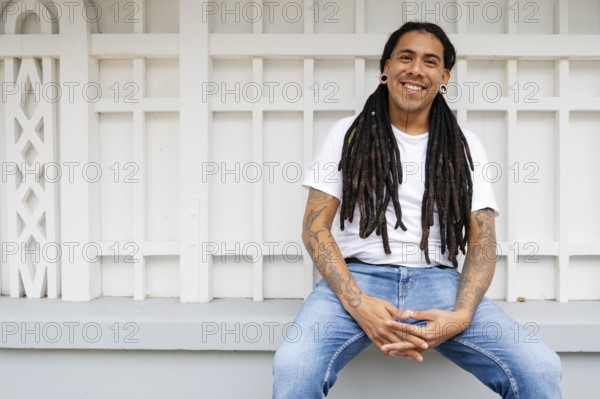 A cheerful man with long dreadlocks and tattoos sits in Barranco, Lima, Peru, exuding a relaxed