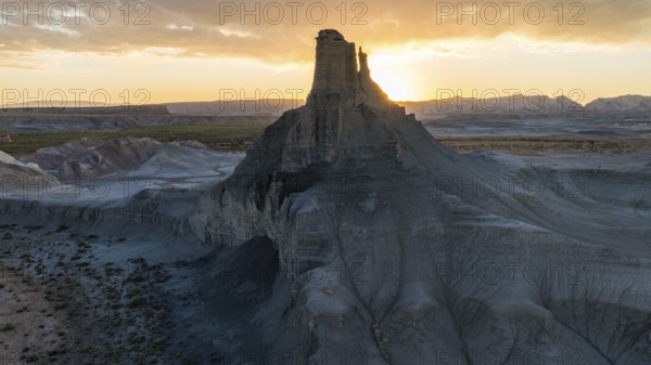 A breathtaking view of the sun setting behind a towering rock formation in Utah, casting a warm