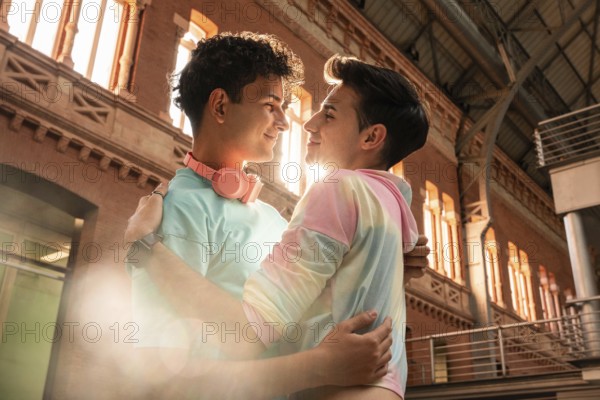 A joyful gay couple embraces lovingly against an urban backdrop, bathed in warm sunlight. The