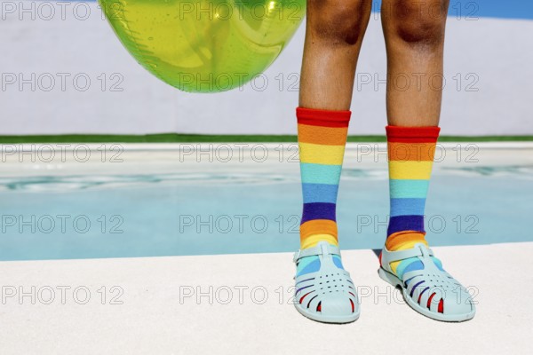 Vibrant rainbow socks and turquoise sandals by a pool, capturing summer's essence. The bright