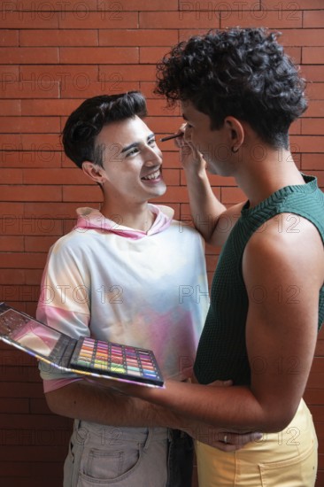 A couple shares a tender moment as one applies makeup to the other with a colorful palette, set