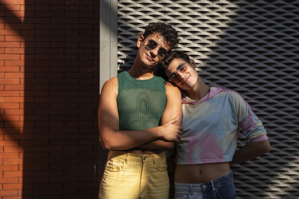 A joyful gay couple in stylish outfits stands together, one leaning on the other affectionately.