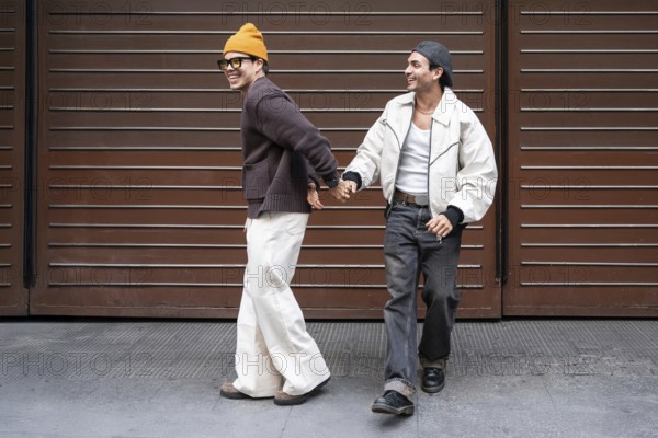 A joyful couple holds hands while walking in an urban setting. They are smiling, showcasing