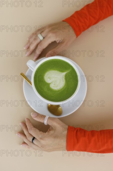 A woman enjoys a matcha latte in a Warsaw cafe Her vibrant orange clothing and trendy rings add