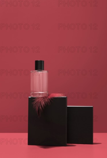 A sleek perfume bottle rests on a black stone stand, elegantly highlighted against a vibrant red